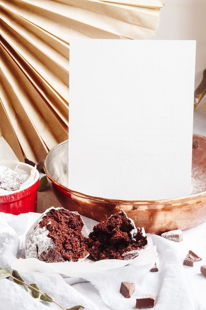 Muffins de chocolate en tazas rojas. Copyspace de papel blanco de maqueta. Pequeña cazuela de cerámica vidriada con tortas marrones sobre fondo gris y blanco.