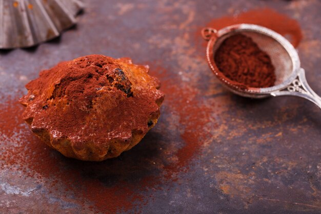 Muffins com mirtilos, cobertos com cacau em pó, sobre um fundo escuro.