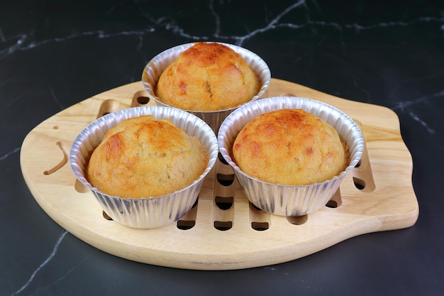 Muffins de banana recém-assados aromáticos nos moldes em uma tábua de pão de madeira