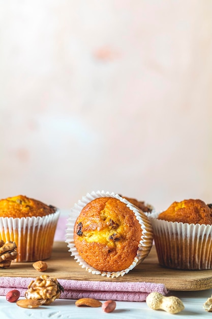 Muffins de caramelo de baunilha em copos de papel em fundo branco de madeira Delicioso cupcake com passas, amêndoas e nozes Bolos de biscoito caseiros Copiar espaço para texto