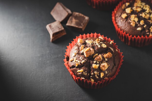 Muffins de chocolate caseiros ou cupcakes polvilhados de nozes em fundo escuro