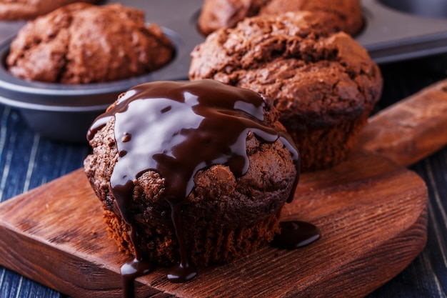 Muffins de chocolate com calda de chocolate em fundo escuro, foco seletivo.