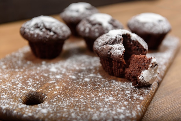 Muffins de chocolate com glacê branco sobre uma tábua polvilhada com açúcar de confeiteiro