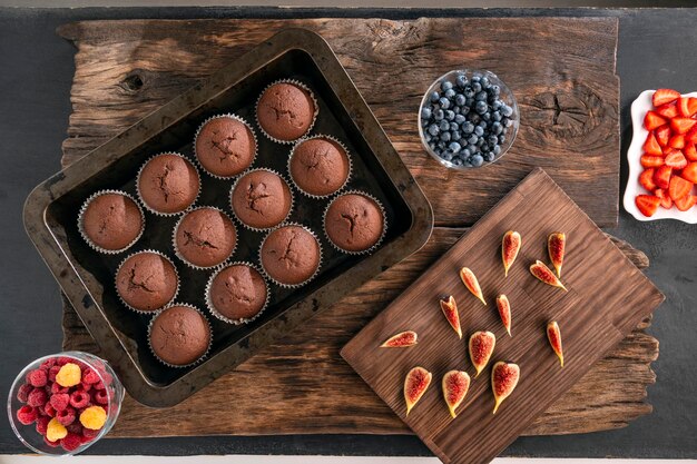 Foto muffins de chocolate recém-assados em assadeiras e frutas e bagas da estação vista superior plana