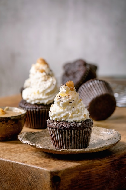 Muffins de cupcakes de chocolate caseiros com creme de manteiga batida branca e caramelo salgado na placa de cerâmica na mesa de madeira.