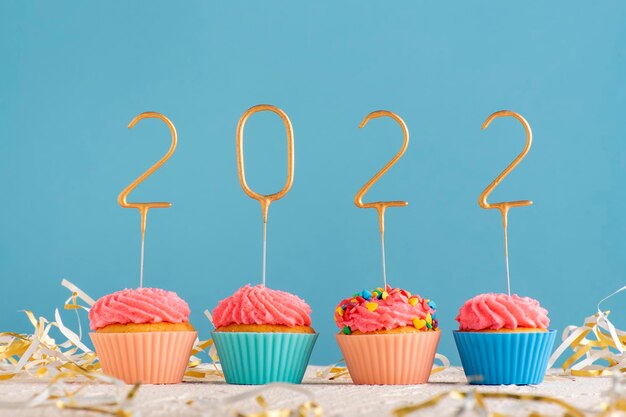 Muffins de férias com creme de manteiga rosa e 2022 números sobre fundo azul. Tema de feliz ano novo.