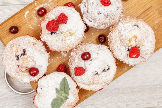 Muffins de frutas caseiros polvilhados com açúcar de confeiteiro e framboesas frescas na tábua de madeira.
