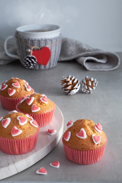 Muffins decorados com corações de açúcar e um copo com coração vermelho sobre fundo cinza claro