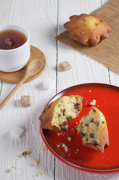 Muffins em um prato vermelho, xícara de chá e cubos de açúcar na mesa de madeira branca