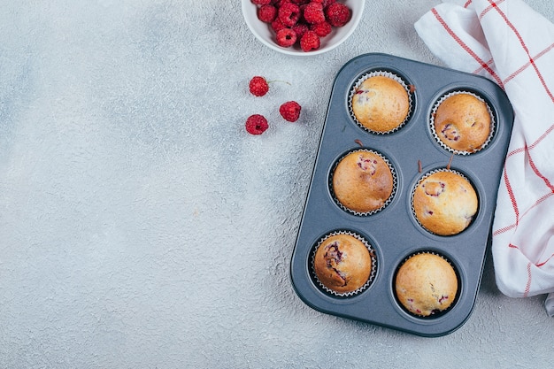 Muffins de frambuesa al horno sobre una rejilla para enfriar sobre mesa de hormigón azul. Vista superior, espacio de copia