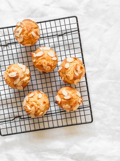 Muffins de maní con pétalos de almendras sobre una rejilla metálica sobre una vista superior de fondo blanco