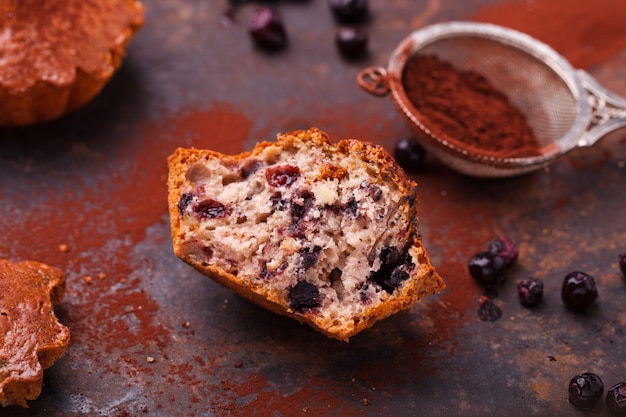 Muffins mit Blaubeeren, mit Kakaopulver belegt, auf dunklem Hintergrund.