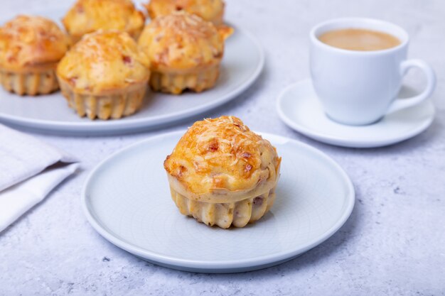 Muffins mit Schinken und Käse. Hausgemachtes Backen. Im Hintergrund ein Teller mit Muffins und einer Tasse Kaffee. Nahansicht.