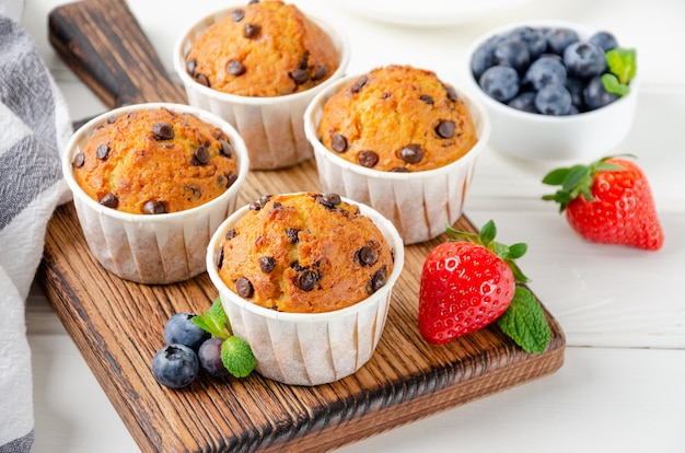 Muffins mit Schokoladenstückchen auf einer hölzernen Bordüre auf einem weißen Hintergrund mit frischen Beeren.