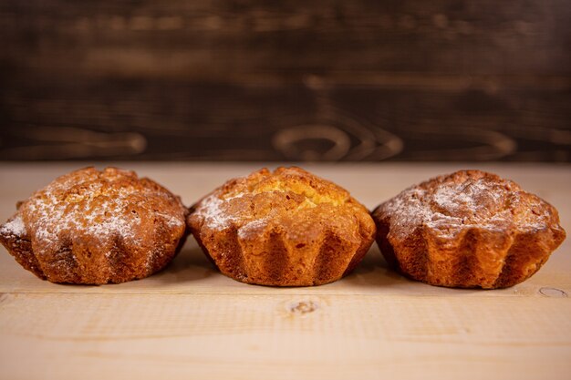 Muffins recém-assados em açúcar de confeiteiro em um fundo de madeira.