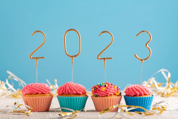 Muffins de vacaciones con crema de mantequilla rosa y números 2023 sobre fondo azul Tema de feliz año nuevo