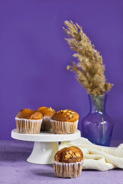 Muffins de vainilla, caramelo y nueces en tazas de papel con plantas de caña sobre un fondo púrpura