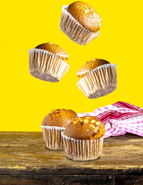 Muffins voadores de baunilha, caramelo, nozes em copos de papel em mesa de madeira perto de fundo amarelo