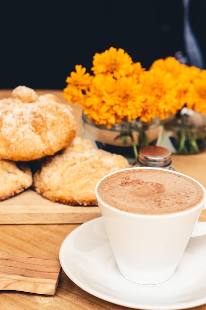 Mug con flores de chocolate, pan e muerto y cempasúchil sobre fondo negro.