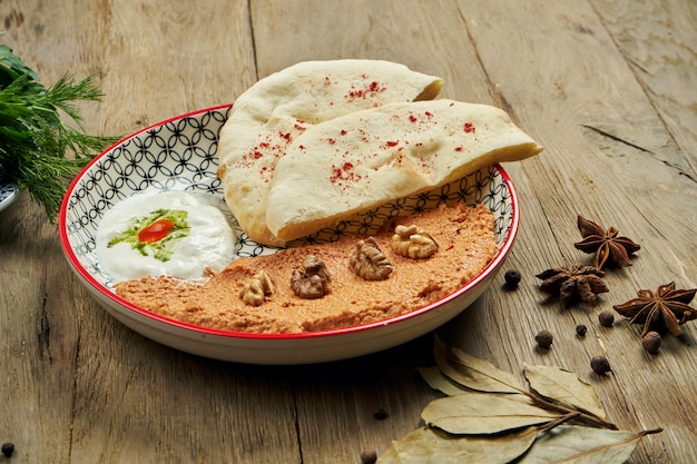 Foto muhammara es un plato clásico de eastren. puré de pimientos y nueces al horno con bazlama y yogurt en un plato de cerámica sobre una superficie de madera.