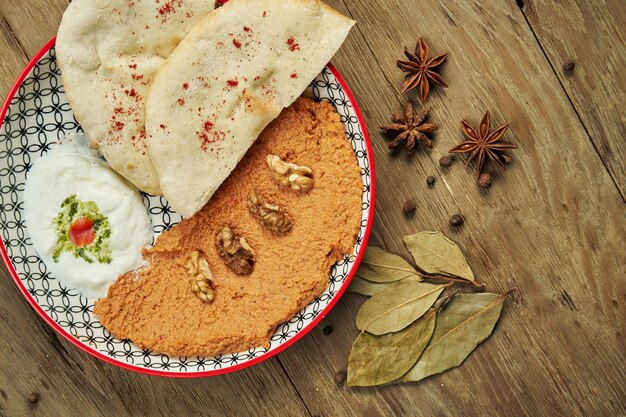 Muhammara es un plato clásico de Eastren. puré de pimientos y nueces al horno con Bazlama y yogurt en un plato de cerámica sobre una superficie de madera.