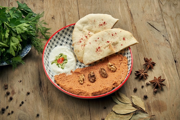 Muhammara es un plato oriental clásico. puré de pimientos y nueces al horno con Bazlama y yogurt en un plato de cerámica sobre una mesa de madera.