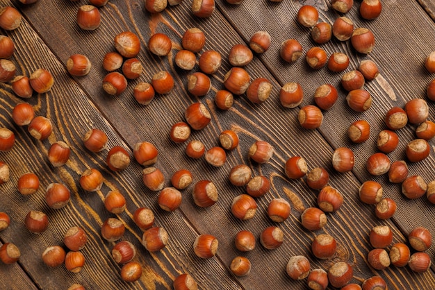Muitas avelãs com cascas espalhadas uniformemente na superfície de madeira marrom