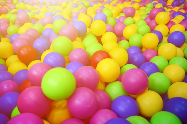 Muitas bolas plásticas coloridas no ballpit dos miúdos em um campo de jogos. Fim, cima, padrão