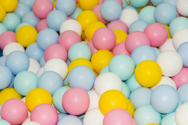 Muitas bolinhas de plástico coloridas na piscina. Brinquedo infantil, rosa, amarelo, azul, branco