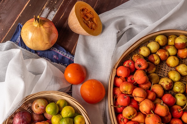 Muitas cores e variedades de frutas estão no prato ou espalhadas na mesa de madeira