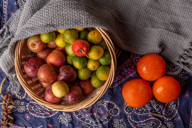 Muitas cores e variedades de frutas estão no prato ou espalhadas na mesa de madeira