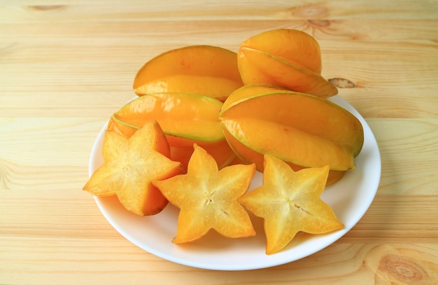 Muitas frutas inteiras maduras de cores vibrantes e frutos de estrela fatiados em um prato branco servido em mesa de madeira