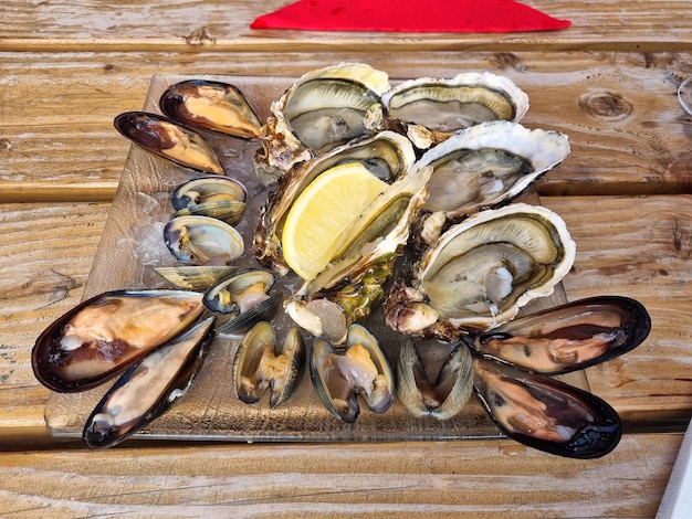 Foto muitas ostras frescas abertas com limão em uma placa de vidro na mesa de madeira escura