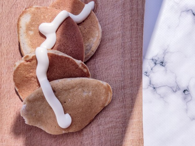 Foto muitas panquecas deliciosas e apetitosas com creme de leite em uma placa de madeira