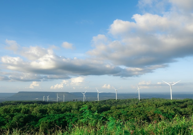 Muitas turbinas eólicas na montanha com fundo de floresta e vale com céu azul e céu nublado