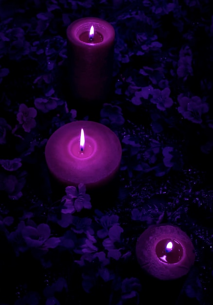 Muitas velas de cores roxas e violetas de veludo mágicas queimam no fundo azul com flores.