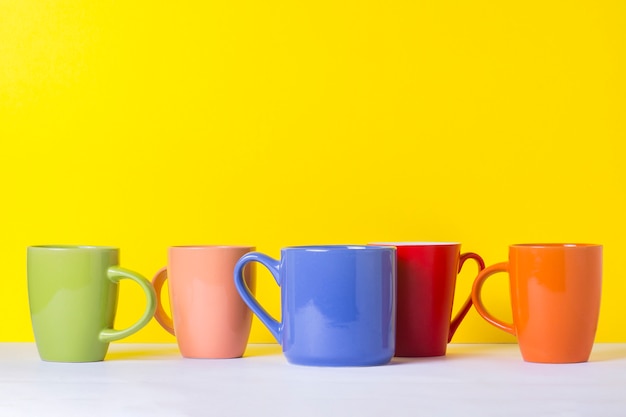 Foto muitas xícaras de café ou chá coloridos em um fundo amarelo. o conceito de uma empresa amigável, uma família numerosa, encontrar amigos para uma xícara de chá ou café.