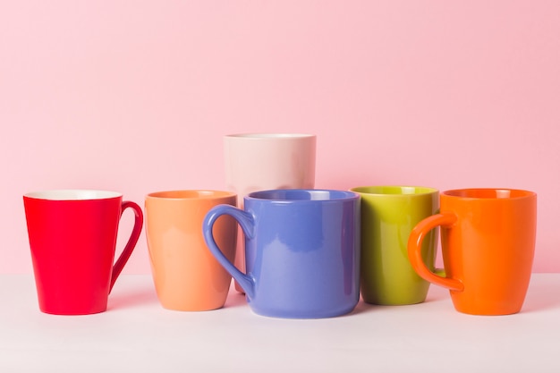 Foto muitas xícaras de café ou chá coloridos em um fundo rosa. o conceito de uma empresa amigável, uma família numerosa, encontrar amigos para uma xícara de chá ou café.