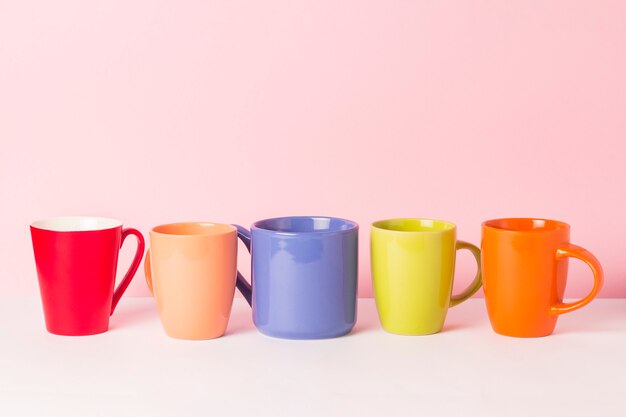 Muitas xícaras de café ou chá coloridos em um fundo rosa. O conceito de uma empresa amigável, uma família numerosa, encontrar amigos para uma xícara de chá ou café.