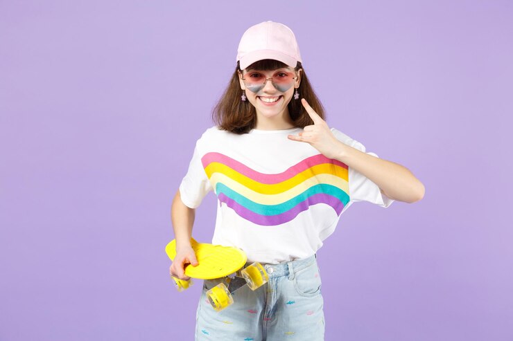 Foto muito adolescente em roupas vívidas, óculos segurando skate amarelo, mostrando chifres para cima gesto isolado em fundo pastel violeta. emoções sinceras de pessoas, conceito de estilo de vida. mock up espaço de cópia.