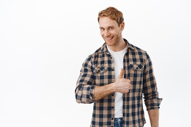 Muito bem. Homem bonito e sorridente com cabelo ruivo, mostrando os polegares para cima para elogiar e elogiar o ótimo trabalho, dar aprovação, dizer que sim, sem problemas, em pé sobre um fundo branco