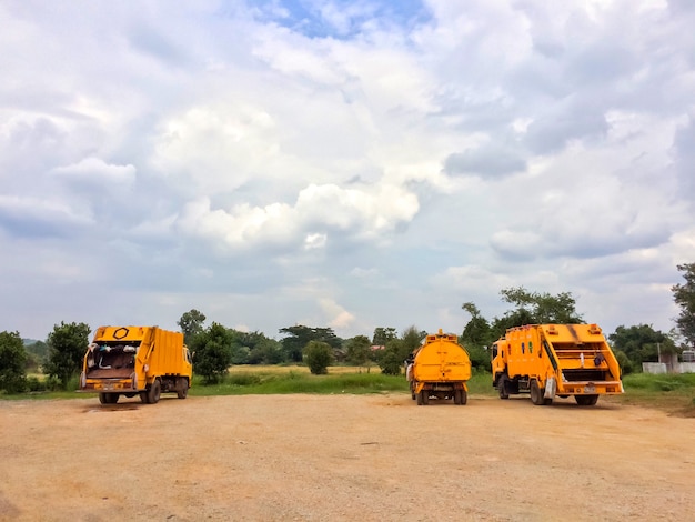 Muito caminhão de lixo amarelo com céu azul e nuvens.