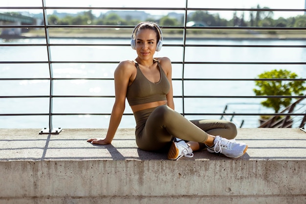 Muito jovem com fones de ouvido faz uma pausa depois de correr na área urbana