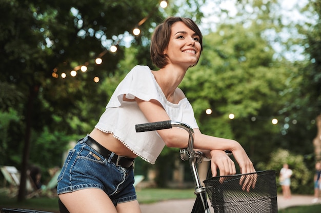 Foto muito jovem com roupas de verão, sentada em uma bicicleta