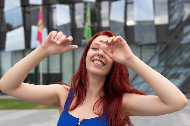 Muito jovem com um maravilhoso senso de humor, cabelo vermelho e um vestido azul em uma rua da cidade rindo para a câmera