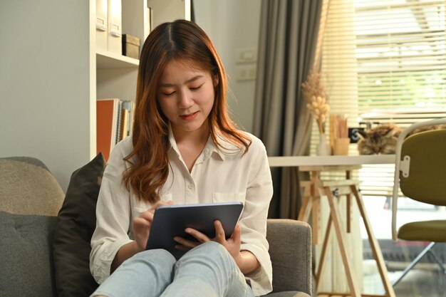 Muito jovem em roupas casuais gosta de navegar na internet sem fio no tablet digital e relaxar no sofá em casa