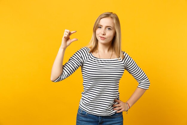 Muito jovem em roupas listradas, olhando para a câmera, gesticulando demonstrando tamanho com espaço de trabalho isolado em fundo amarelo laranja. Emoções sinceras de pessoas, conceito de estilo de vida. Mock up espaço de cópia.