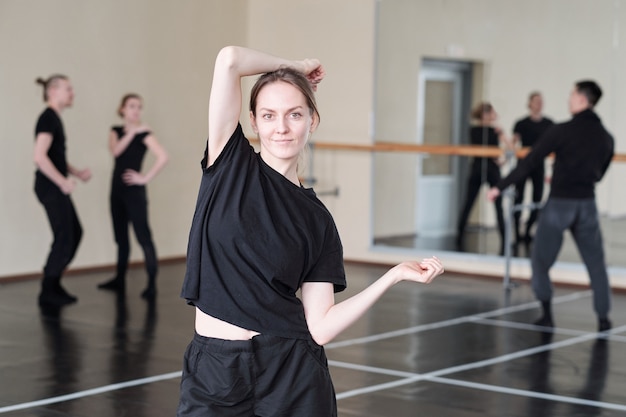 Muito jovem estudante do curso de dança de balé moderno com roupa esportiva preta em pé enquanto faz exercícios