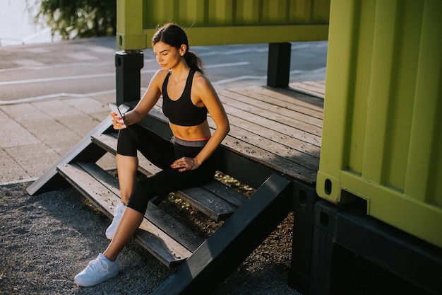 Muito jovem fazendo uma pausa durante o exercício fora e usando o celular