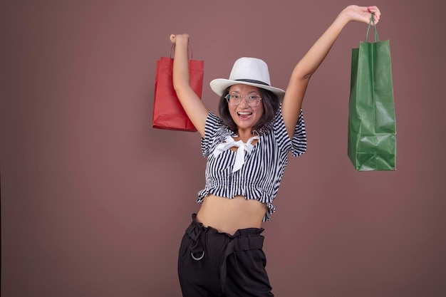 Muito jovem garota asiática com sacolas de compras e chapéu em fundo liso